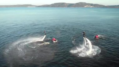 Deniz suyu üzerinde jet paketleri ile hile yapan sportif erkekler