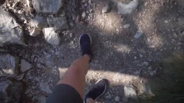 Yukarıdan görüntüleyin. Şort ve spor ayakkabılı bir adam yürüyüş parkuruna gider. Yol taşlarla ve ağaç kökleriyle dolu..