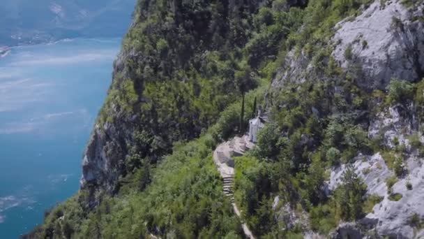 Vista aérea. Hermosas montañas rocosas. Una pequeña iglesia se encuentra justo en el acantilado. Santa Barbara, una iglesia no muy lejos de Riva del Garda . — Vídeos de Stock