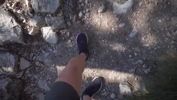Vista desde arriba. Un hombre en pantalones cortos y zapatillas de deporte va en una ruta de senderismo. El camino está lleno de piedras y raíces de árboles . — Vídeos de Stock