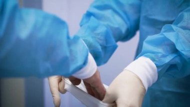 Bir hemşire doktora lastik eldiven takmaya yardım eder. Karmaşık bir operasyona hazırlanmak, sterilite koşullarına ve diğer güvenlik protokollerine uymak önemlidir.