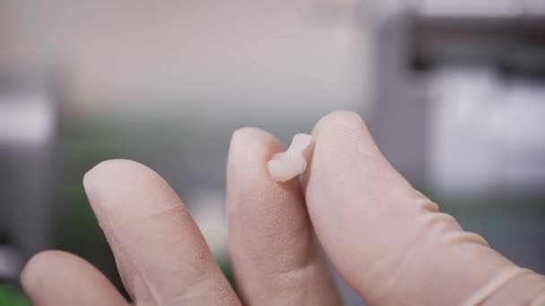 Macro inyección de una corona dental en las manos de un médico. El dentista sostiene en sus manos una corona dental hecha con precisión, pronto se implantará en la cavidad oral de los pacientes . — Vídeo de stock