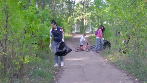 女性と子供のグループは、森の中でゴミを収集します。ボランティアは黒いビニール袋にプラスチックやその他の廃棄物を集めます。人々は環境に対して責任を負う. — ストック動画