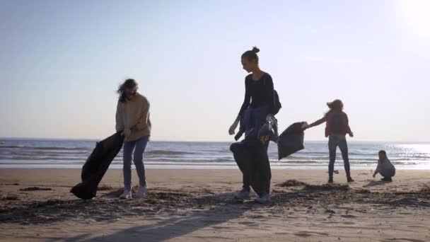 Děvčata dobrovolníci čistí pobřeží před odpadky. Ženy zásobují odpadky na břeh v černých taškách. Ekologická dobrovolná akce.