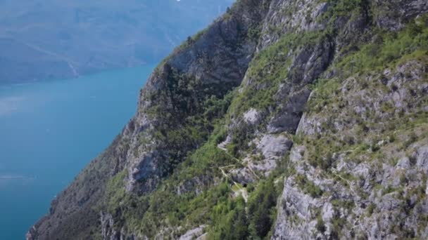 Drone sta volando lungo l'alto monte vicino al famoso lago di Garda, mostrando piccolo edificio in grotta di scogliera nella giornata estiva — Video Stock