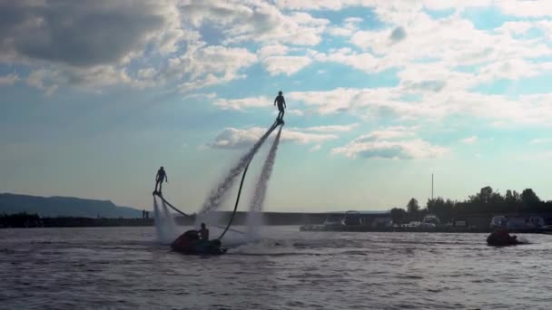 Two flyboardists are riding on lake in daytime, silhouette view against blue sky with clouds — Stock Video