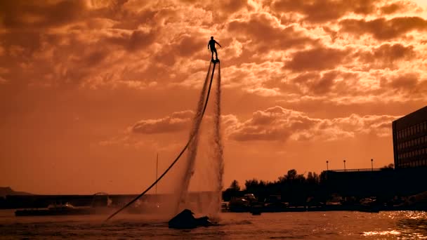 Man is practicing flyboarding in sunset time on sea, moving over water surface on flows — Stock Video