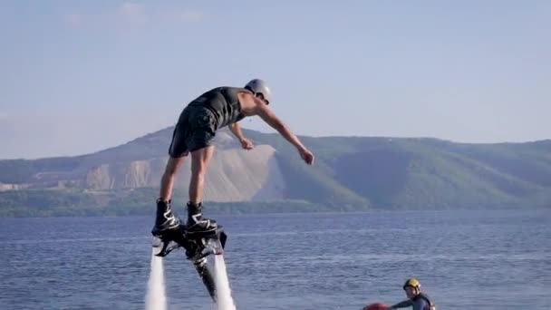 Man is flying on flyboard over sea surface, water flows are lifting him up in summer day, drops are splashing around — Stock Video
