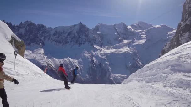 A snowboardosok gyönyörű alpesi lejtőkön lovagolnak. Napos téli nap. — Stock videók