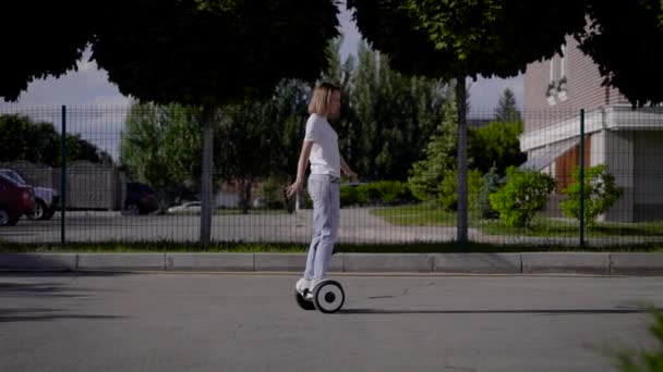 Una ragazza snella cavalca un maialino giroscopio lungo una strada cittadina. Trasporto elettrico moderno. — Video Stock