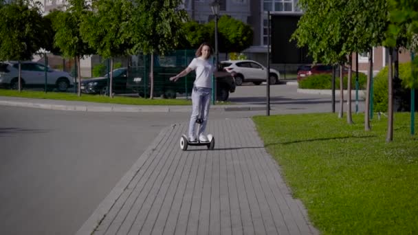 A slender young girl rides a gyro scooter along a city street. Modern electric transport. — Stock Video