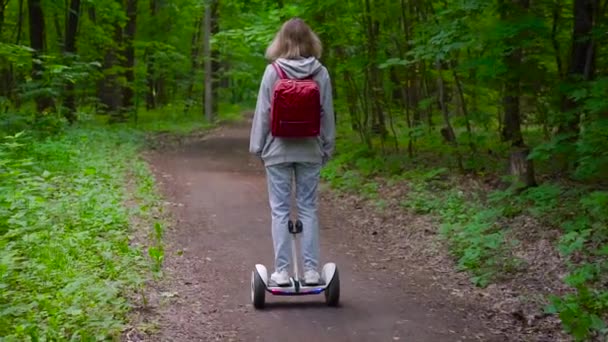 Eine Frau fährt mit einem elektrischen Tragschrauber auf einem Waldweg. Das Mädchen hat einen roten Rucksack und eine helle Jeans. — Stockvideo