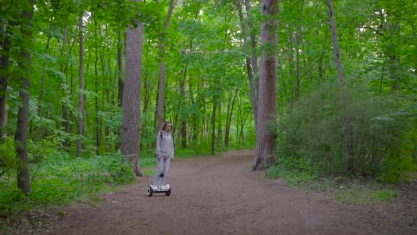 A girl dressed in casual rides through the forest on a gyro scooter. Modern electric transport. — Stock Video