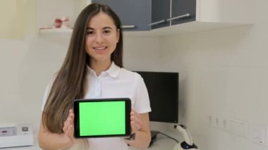 Kadın elleri, dişçinin ofisinde yeşil ekranlı siyah bir tablet kullanıyor. Krom anahtar. Kapat.