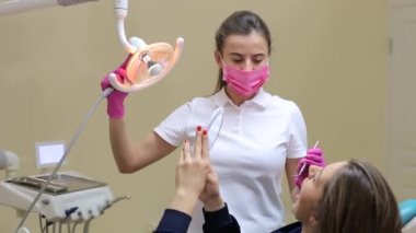 Muayene ve diş temizliği için bir hastanın portresi. Dişçi aynalı genç bir kadının dişlerini kontrol ediyor..