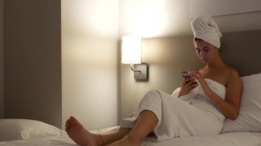 Güzel, seksi genç bir kadın duş aldıktan sonra yatağında uzanıyor. Kafasında havluyla cep telefonu, sayfaları kaydırıyor ve internette sörf yapıyor.