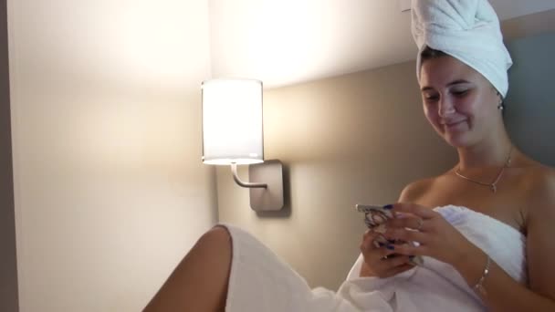 漂亮性感的年轻女人洗完澡 头戴毛巾 躺在被窝里 用智能手机 滚动页面和上网 — 图库视频影像