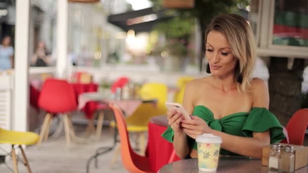 携帯電話を持った美しい女性が屋外のカフェのテーブルに座ってコーヒーを飲みながら — ストック動画