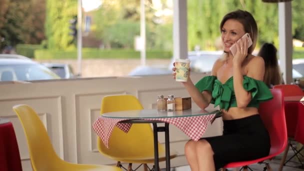 ある朝 美しいエレガントな女性が屋外のカフェでコーヒーを飲みながら電話で彼女の友人を呼び出し 笑って喜びます — ストック動画