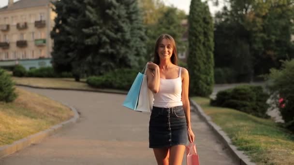 買い物袋付きの幸せな若い女性は成功した買い物の後に家に帰る — ストック動画