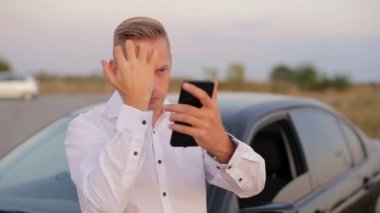 Yakışıklı gülümseyen iş adamı arabanın yanında duruyor ve cep telefonu kullanıyor..