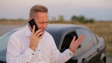 Adam gergin bir şekilde şehrin dışındaki arabanın yanında telefonla konuşuyor.