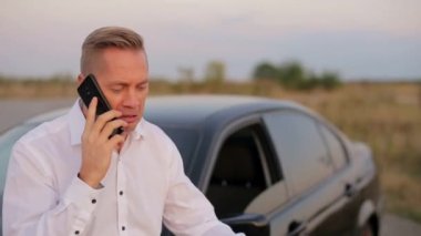 Adam gergin bir şekilde şehrin dışındaki arabanın yanında telefonla konuşuyor.