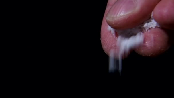 Ruka rozptyluje sůl na černém pozadí. — Stock video