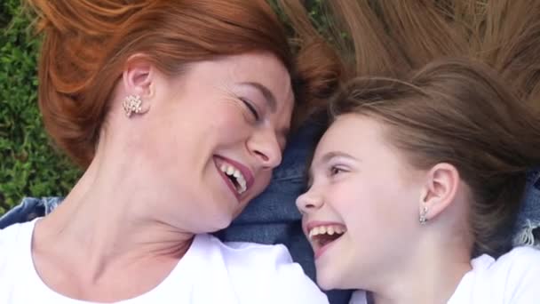 Mom and daughter lie on the green grass in a suburban park. — Stock Video