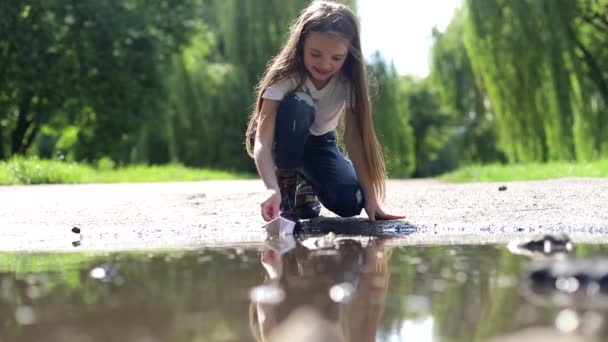Маленькая девочка играет в луже с бумажной лодкой, замедленная съемка — стоковое видео