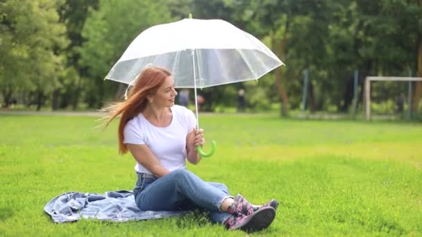 En ensam kvinna sitter i en stadspark och gömmer sig från solen under ett paraply. — Stockvideo