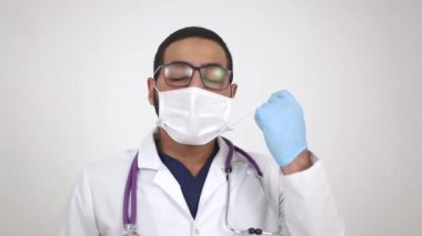 Arap genç doktor kameraya gülümseyen tıbbi maskeyi çıkarıyor..