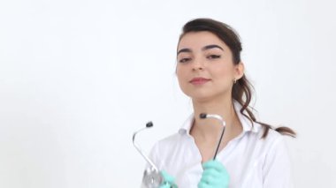 Beyaz önlüklü, steteskoplu gülümseyen doktor kız beyaz arka planda duruyor ve kameraya bakıyor. Meslek ve hastane kavramı, Avrupalı kadın doktor
