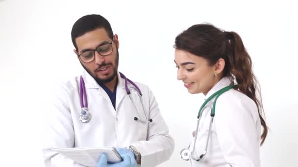 Dois jovens médicos, um homem e uma mulher de casacos brancos, conversam usando um tablet digital . — Vídeo de Stock