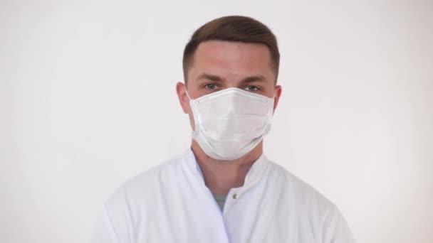 若いヨーロッパの医師は、カメラを見て笑いながら、医療用マスクを脱ぎます. — ストック動画