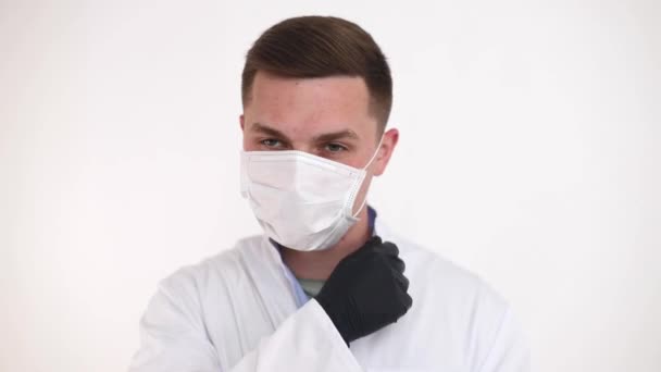 Um médico em uma máscara médica faz observações, apontando um dedo para o lado. Jovem médico de sucesso na medicina moderna — Vídeo de Stock