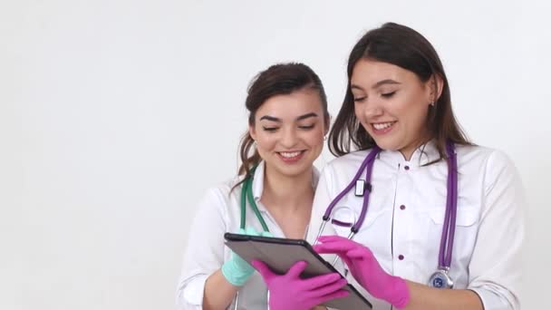 Las estudiantes pasantes usan una tableta. Enfermeras felices ríen alegremente y navegan por las redes sociales . — Vídeos de Stock