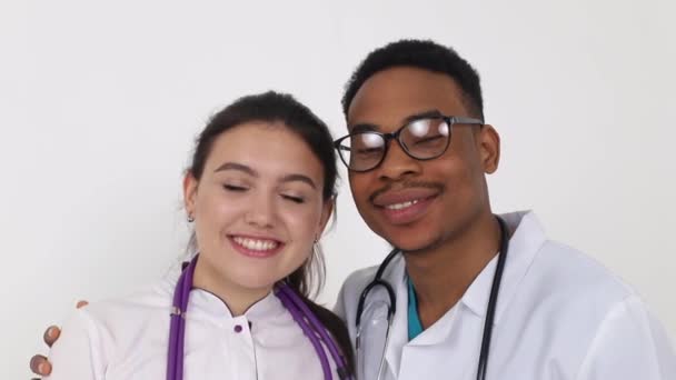 Два молодых врача разных рас, выглядящих и улыбающихся — стоковое видео