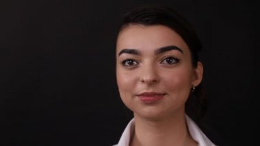 Siyah arka planda esmer bir kızın yüzü, bir kadın kameraya gülüyor.