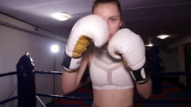 Kız boksör aktif olarak kameranın önünde yumruklarını sallıyor, boks antrenmanı yapıyor.