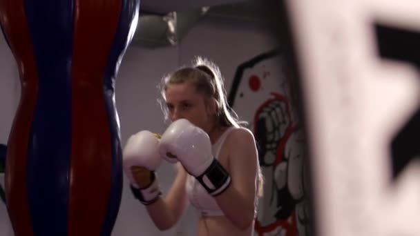 Сильная женщина в боксёрских перчатках бьёт сумку в спортзале. Женский бокс. — стоковое видео