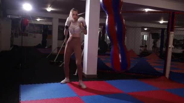 Сильная женщина в боксёрских перчатках бьёт сумку в спортзале. Женский бокс. — стоковое видео