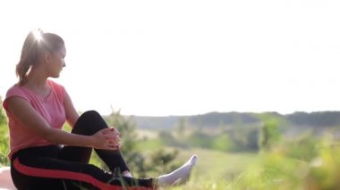 Gün batımında parkta havluyla tahta egzersizleri yapan genç bir kadın..