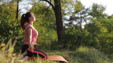 Gün batımında parkta havluyla tahta egzersizleri yapan genç bir kadın..