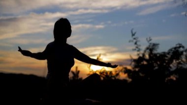 Şehir parkında yoga yapan genç bir kadının silueti.