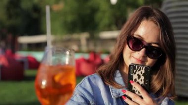 Bir kadın portakal kokteyli içer ve akıllı telefonuyla fotoğrafını çeker.