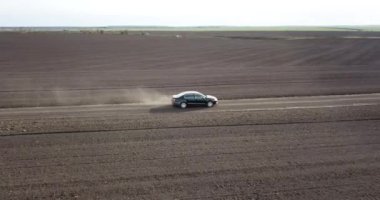 Araba kırsalda yol boyunca yarışıyor ve tozlu bir manzara esiyor.