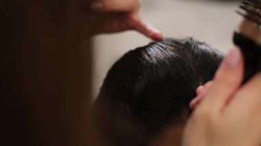 Profesyonel tımar hizmeti sırasında saç fırçalayan stilistin yakın çekimi.