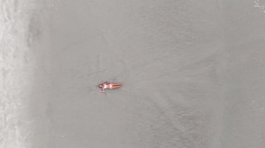 Geniş kumsalda güneşlenen bir kadının hava görüntüsü. Drone görünümü.