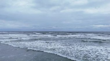 Bulutlu bir günde kıyıya doğru gelen güçlü dalgaların geniş bir görüntüsü. Ufuk ve deniz atmosferli doğal deniz manzarası.